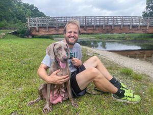 dog-walking-park A man sitting on the ground, arm around a dog, with a bridge in the background.