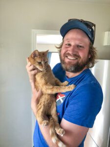 pet-sitting-cat A man is smiling at the camera holding an orange cat.