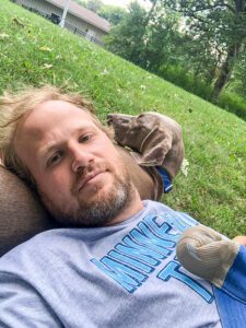 pet-sitting-dog-in-grass A man and a dog are laying in a grassy lawn.