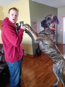 pet-sitting-dog-in-house A man is holding the paws of a standing large Great Dane.
