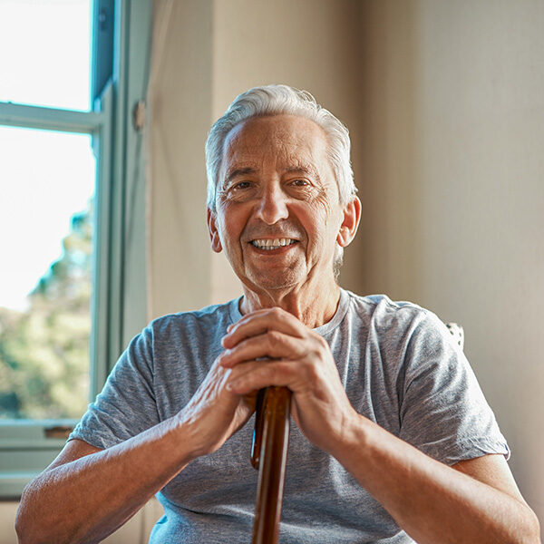 family-check-in-services An elderly gentleman with a cane looks at the camera smiling.
