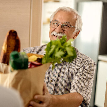 home-people-services An elderly man is being handed a bag of groceries.